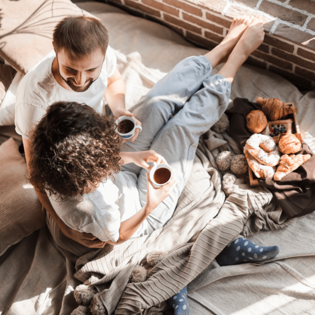 A couple sits together with cups of coffee in a living room.