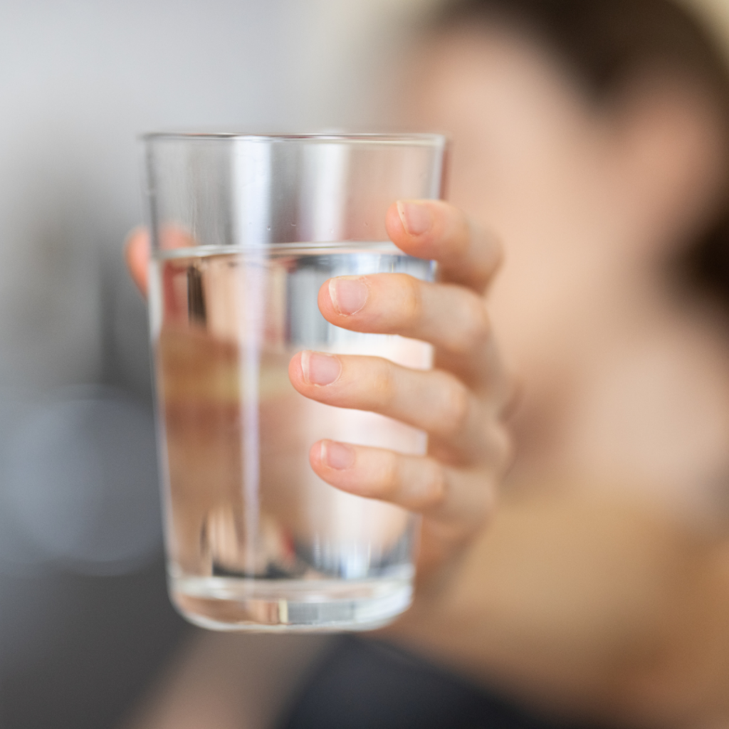 A hand holds up a clear glass of water. 